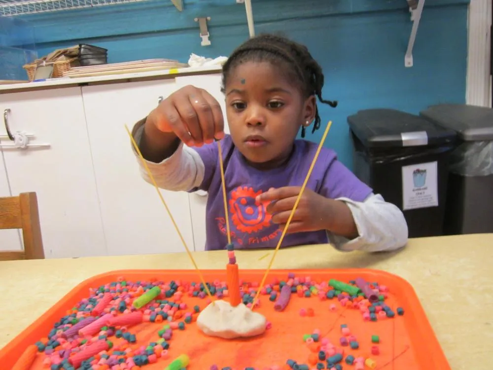 A child creating a sculpture from play dough, beads and spaghetti