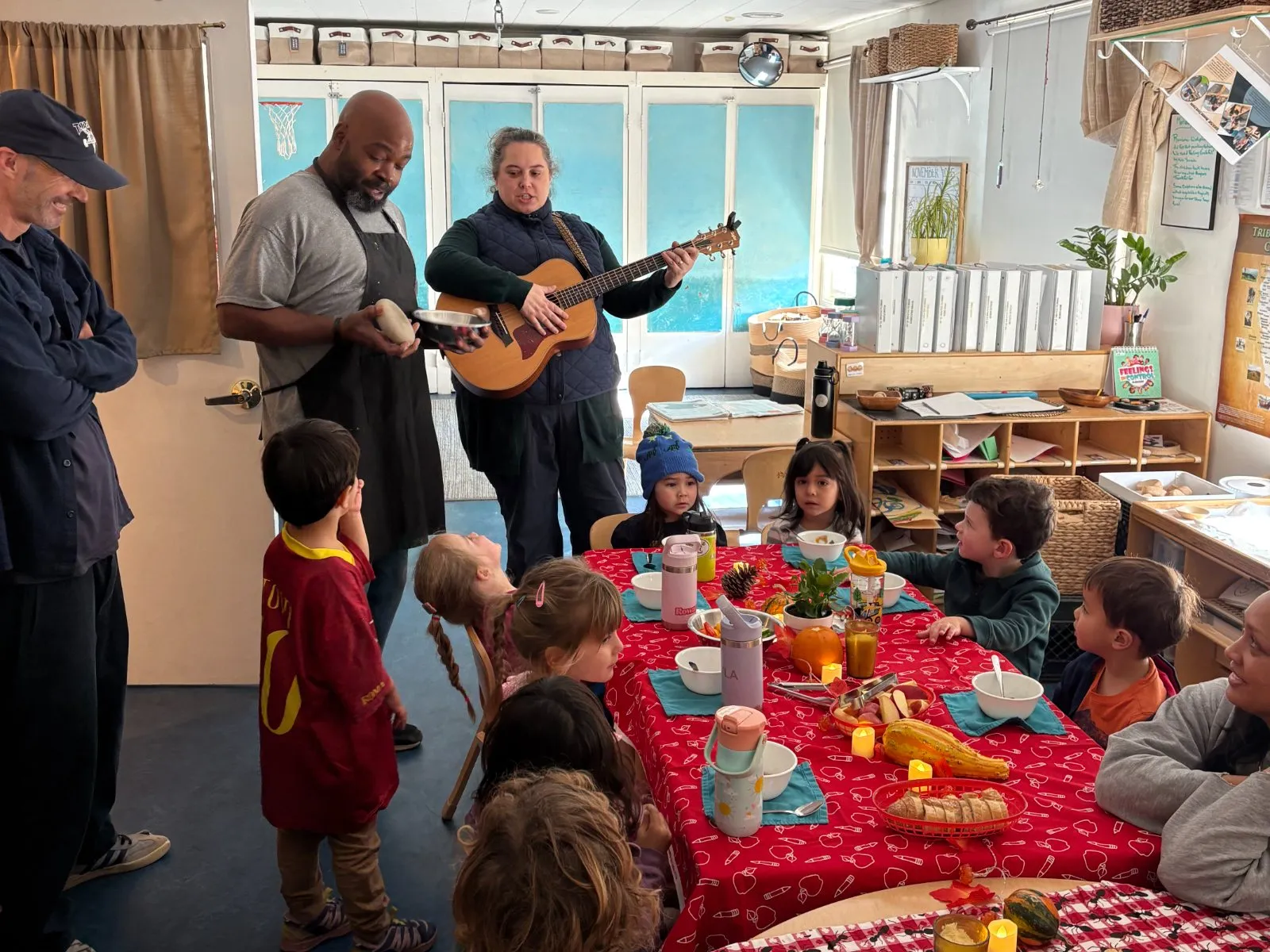 Teachers playing guitar and singing at a harvest lunch with children