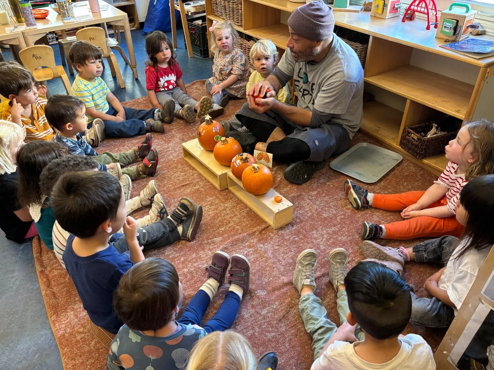 A teacher and children sitting in a circle with pumpkins